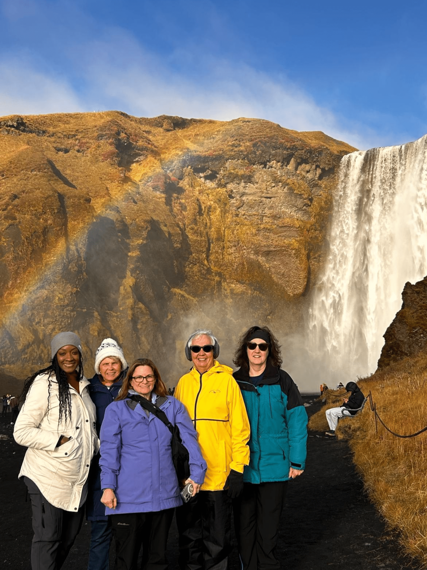 Women Travel Abroad in front of waterfall in Iceland with rainbow in background Women Travel Abroad in front of waterfall in Iceland with rainbow in background