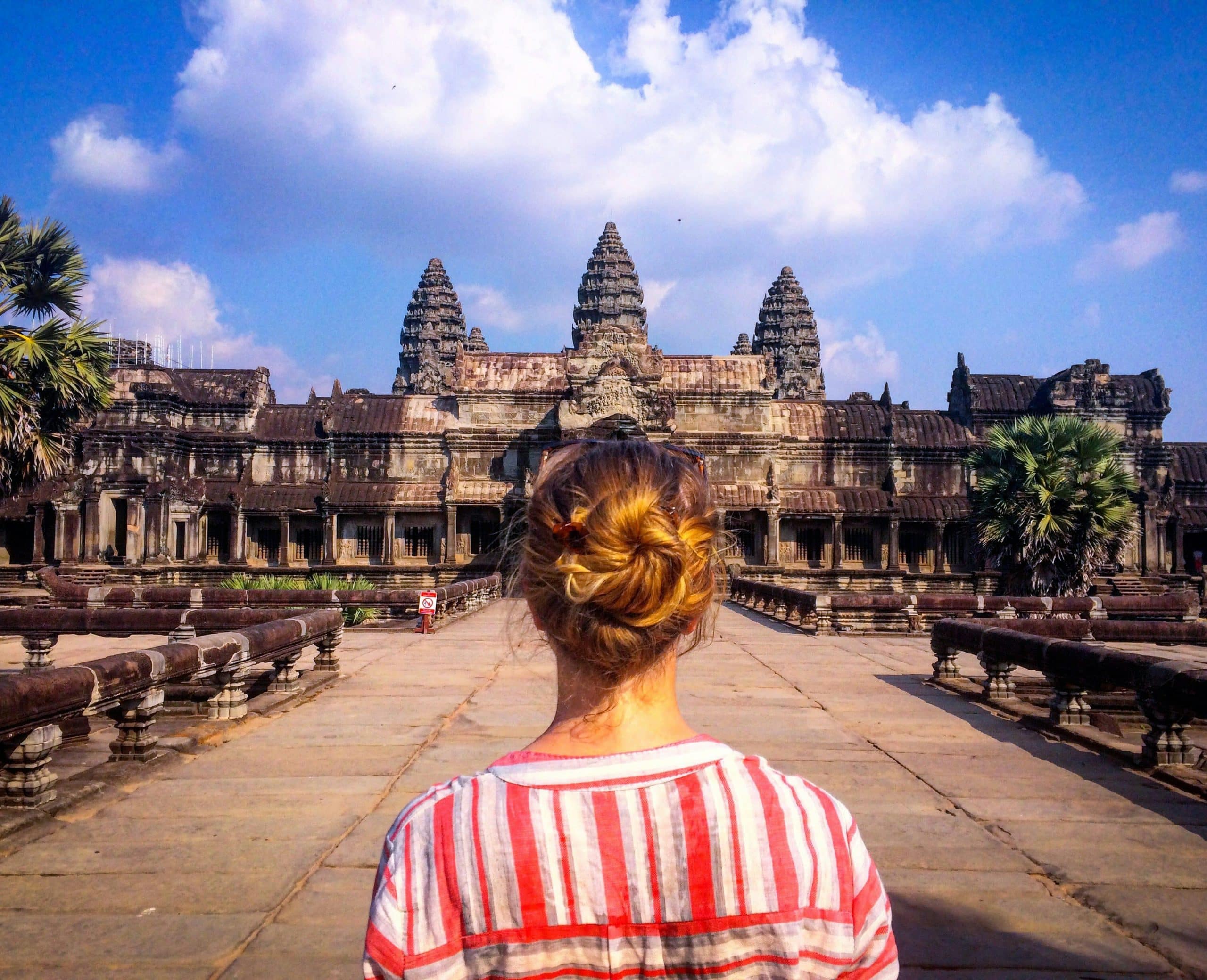 Solo female traveler standing in front of the ancient temple ruins of Angkor Wat at sunrise Solo female traveler standing in front of the ancient temple ruins of Angkor Wat at sunrise