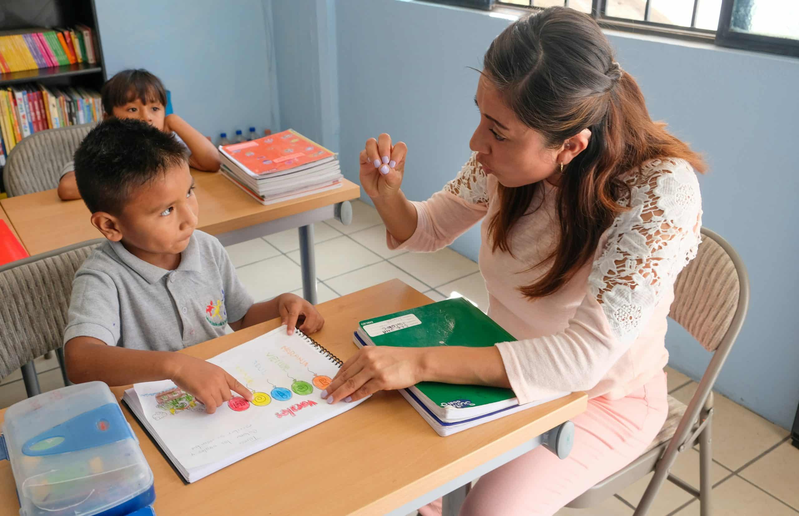 Solo female traveler sitting with a young student in a classroom, smiling and teaching Solo female traveler sitting with a young student in a classroom, smiling and teaching
