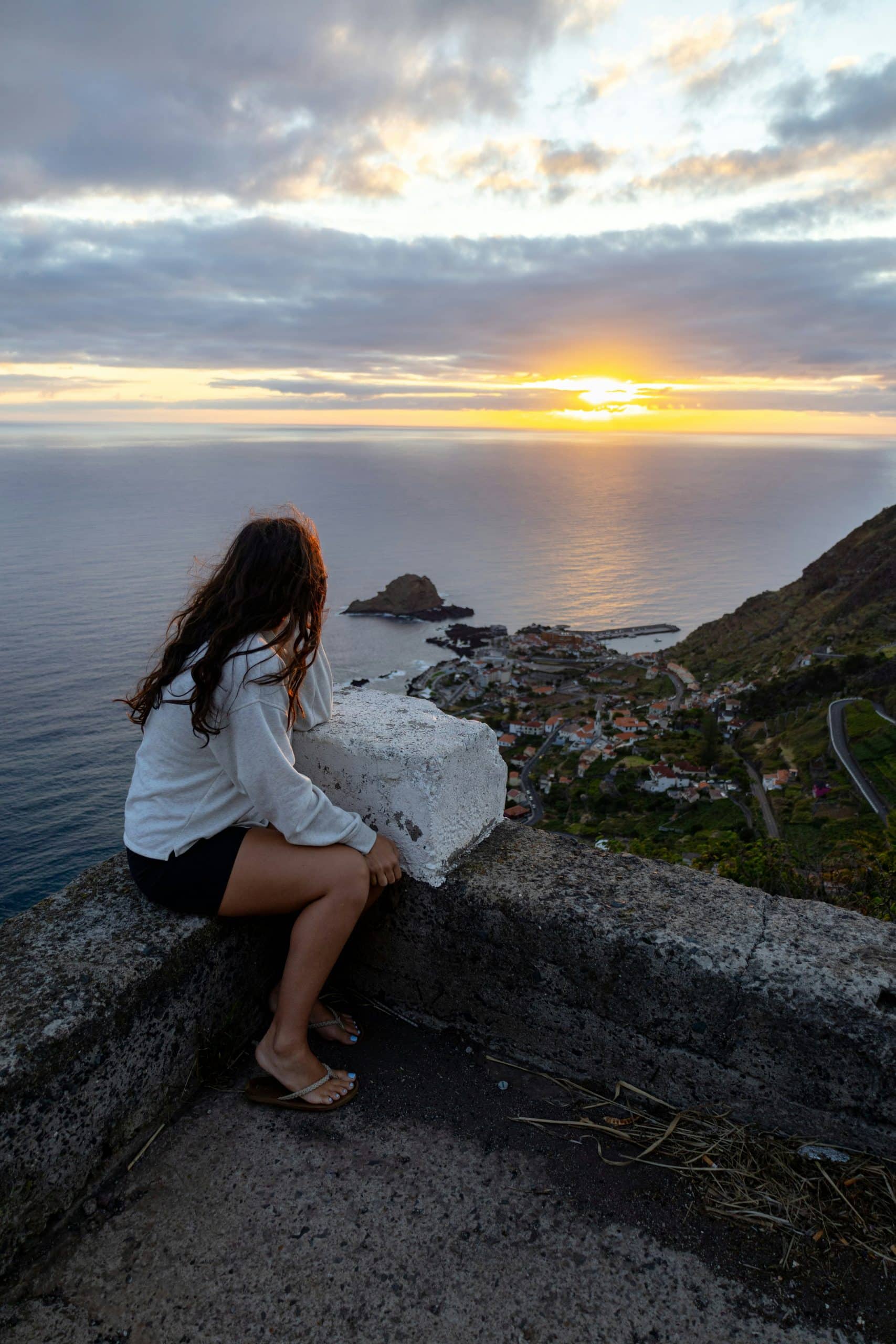 Solo female traveler sitting on a cliff overlooking the ocean at sunset Solo female traveler sitting on a cliff overlooking the ocean at sunset